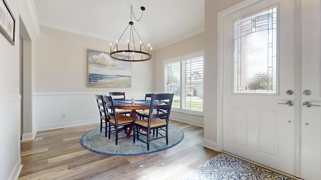 dining area with a wainscoted wall, a chandelier, crown molding, and light wood finished floors