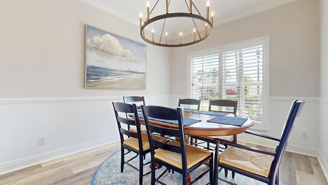 dining area featuring an inviting chandelier, light wood-style flooring, crown molding, and a wainscoted wall