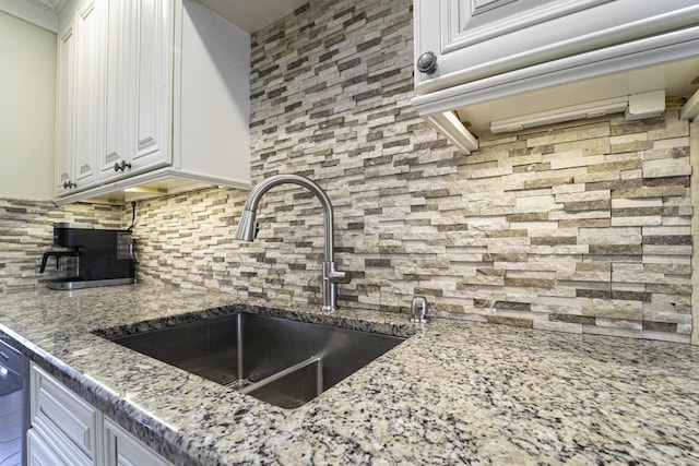 kitchen featuring backsplash, light stone countertops, white cabinetry, and a sink