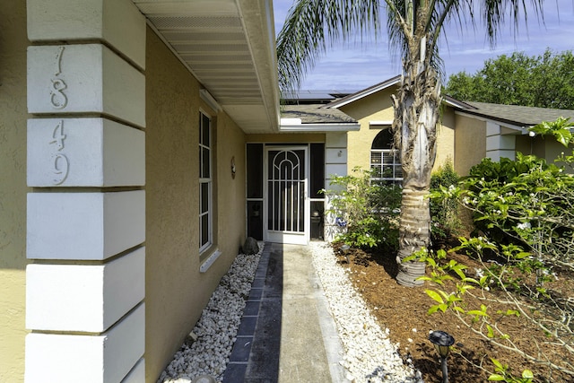 doorway to property featuring roof mounted solar panels, stucco siding, and a shingled roof