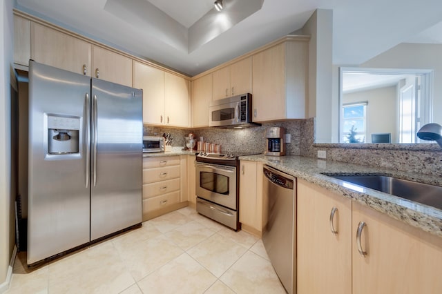 kitchen featuring light brown cabinetry, decorative backsplash, stainless steel appliances, and a sink