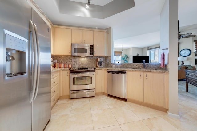 kitchen featuring a tray ceiling, stainless steel appliances, backsplash, and light brown cabinetry