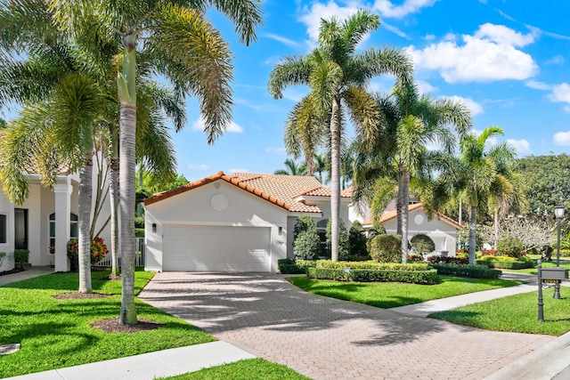 mediterranean / spanish-style home featuring stucco siding, a front lawn, driveway, a tile roof, and an attached garage