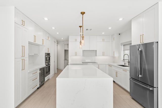 kitchen featuring visible vents, a center island, freestanding refrigerator, white cabinets, and a sink