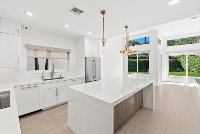 kitchen featuring visible vents, a sink, a center island, freestanding refrigerator, and white cabinets