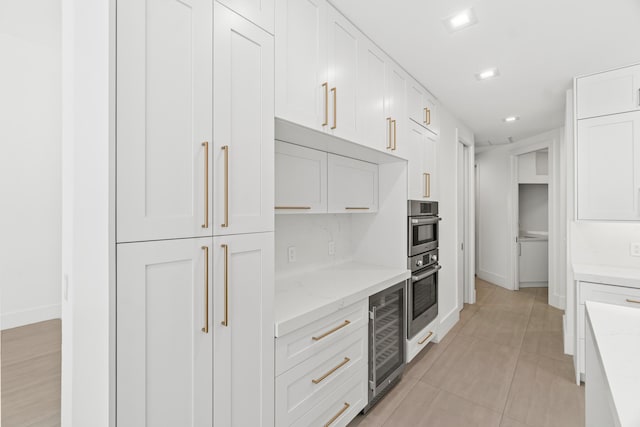 kitchen with light stone counters, white cabinetry, wine cooler, light tile patterned flooring, and baseboards