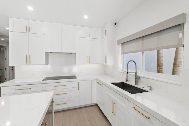 kitchen with light stone countertops, a sink, decorative backsplash, white cabinets, and black electric cooktop