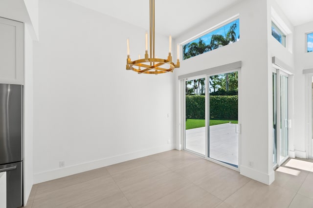 unfurnished dining area featuring baseboards, plenty of natural light, a chandelier, and a towering ceiling