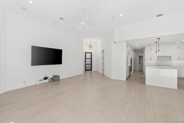 unfurnished living room featuring recessed lighting, ceiling fan with notable chandelier, visible vents, and baseboards