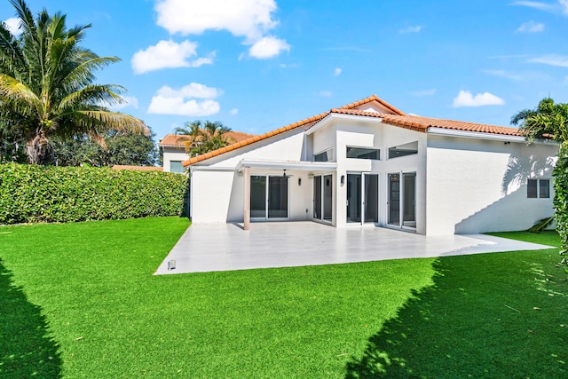 back of property with stucco siding, a tiled roof, a lawn, and a patio