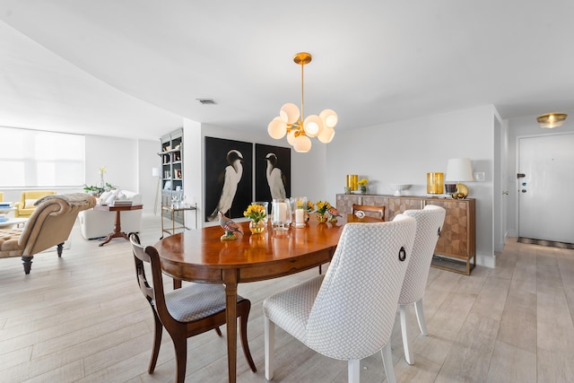 dining area featuring light wood finished floors, visible vents, and an inviting chandelier