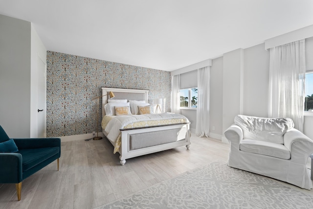 bedroom with multiple windows, an accent wall, baseboards, and wood finished floors