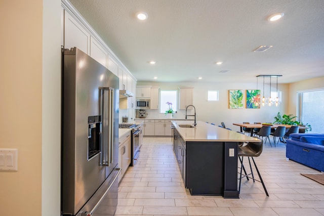 kitchen featuring visible vents, high quality appliances, a kitchen island with sink, white cabinets, and light countertops