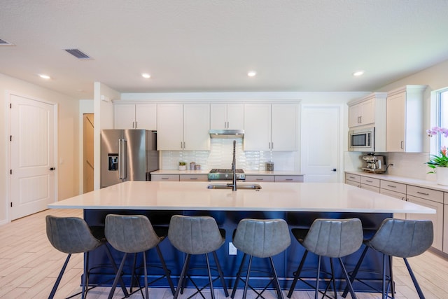 kitchen with visible vents, a large island, light wood-style flooring, under cabinet range hood, and stainless steel appliances