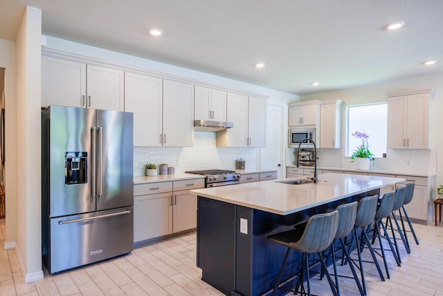 kitchen featuring a breakfast bar, a sink, under cabinet range hood, stainless steel appliances, and decorative backsplash