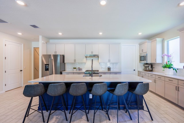 kitchen with a sink, light countertops, a kitchen island with sink, and stainless steel appliances