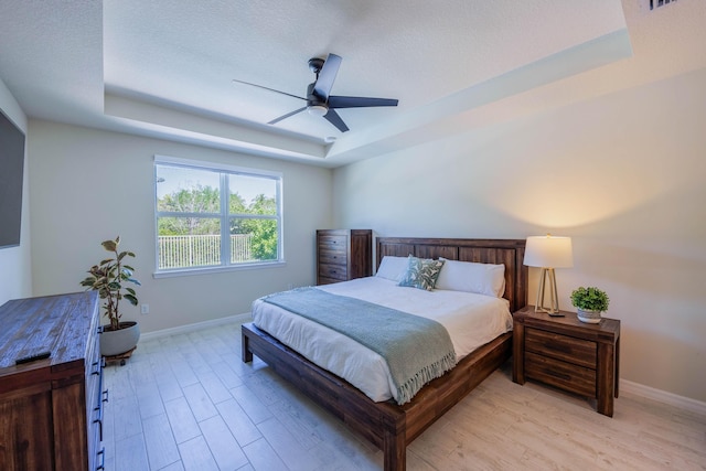 bedroom with a tray ceiling, baseboards, light wood-style floors, and ceiling fan