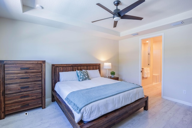 bedroom with baseboards, visible vents, a tray ceiling, ensuite bathroom, and light wood-type flooring