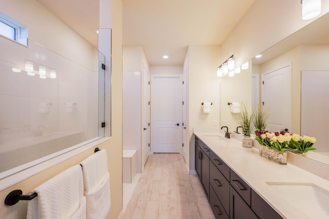 bathroom with double vanity, walk in shower, wood finished floors, and a sink