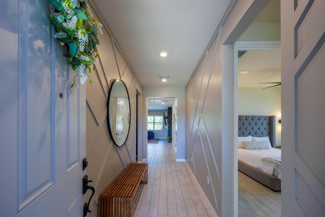 hallway with baseboards, visible vents, light wood finished floors, and a textured ceiling