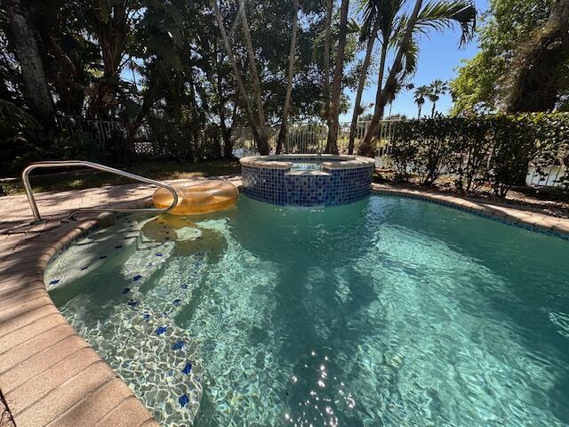 view of pool featuring a pool with connected hot tub and fence