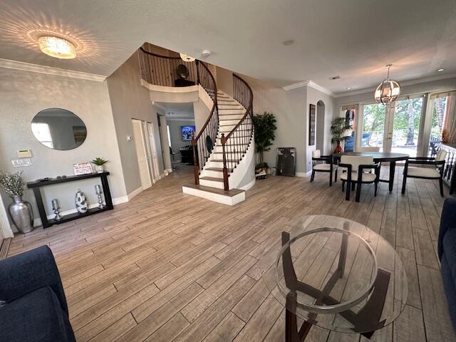 interior space with baseboards, a chandelier, stairs, ornamental molding, and wood finished floors