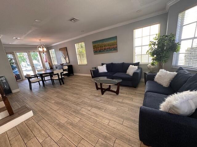 living area featuring light wood-type flooring, baseboards, visible vents, and crown molding