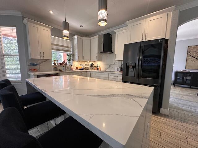 kitchen with decorative backsplash, crown molding, wall chimney range hood, light wood-type flooring, and black fridge