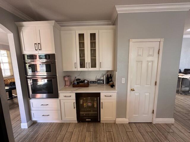 bar with stainless steel double oven, light wood-type flooring, wine cooler, and ornamental molding