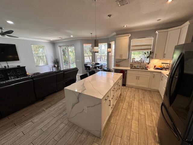 kitchen featuring light wood finished floors, a sink, black appliances, crown molding, and open floor plan