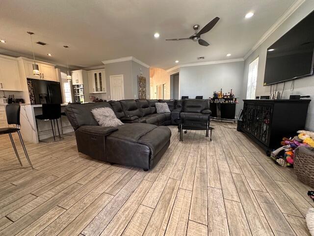 living room featuring recessed lighting, light wood-type flooring, crown molding, and ceiling fan with notable chandelier