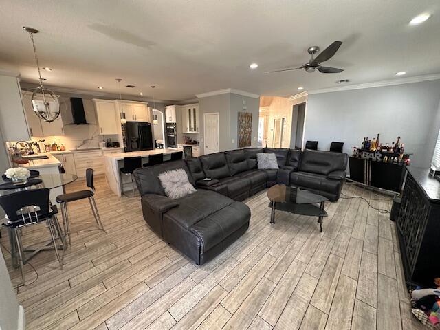 living area featuring light wood finished floors, recessed lighting, ceiling fan with notable chandelier, and ornamental molding