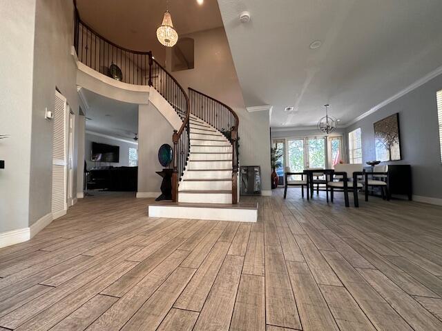 foyer featuring stairway, wood finished floors, baseboards, crown molding, and a chandelier