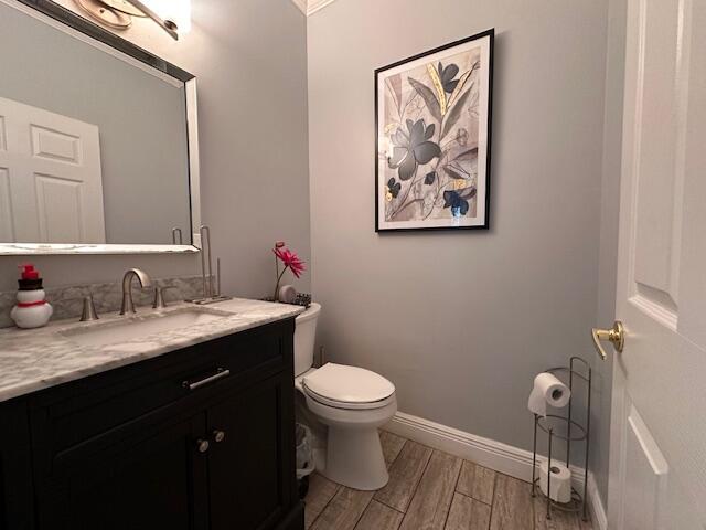 half bath featuring vanity, toilet, wood finished floors, and baseboards