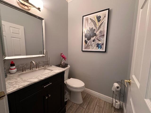 bathroom with baseboards, toilet, wood finished floors, and vanity