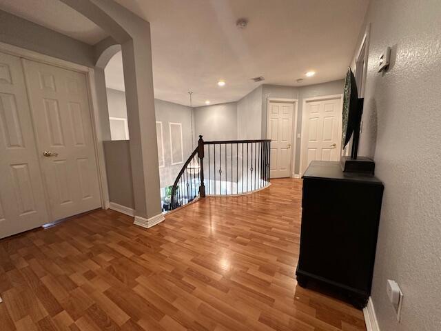 hall featuring an upstairs landing, wood finished floors, arched walkways, baseboards, and a textured wall