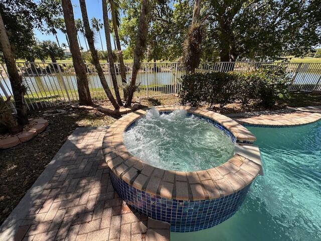 view of swimming pool featuring an in ground hot tub, a water view, and fence