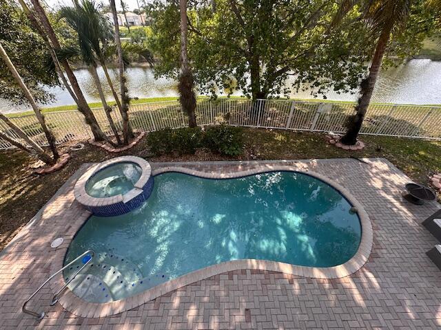 view of swimming pool featuring a patio area, a pool with connected hot tub, a fenced backyard, and a water view