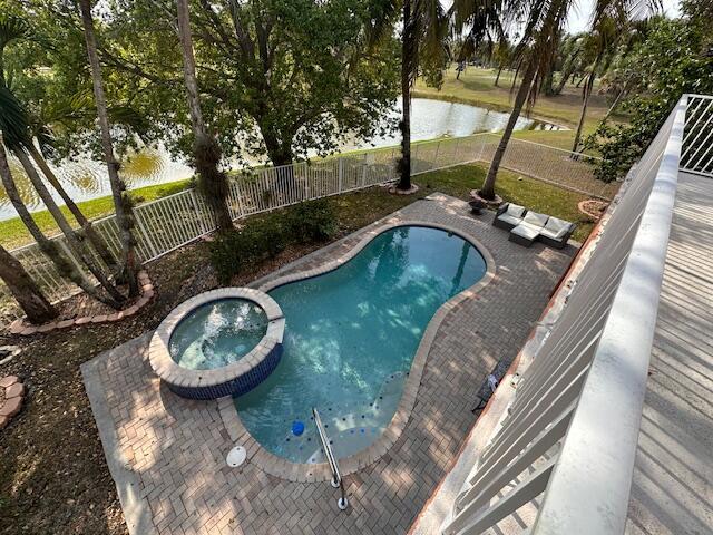 view of pool featuring a patio, a fenced backyard, a water view, and a pool with connected hot tub