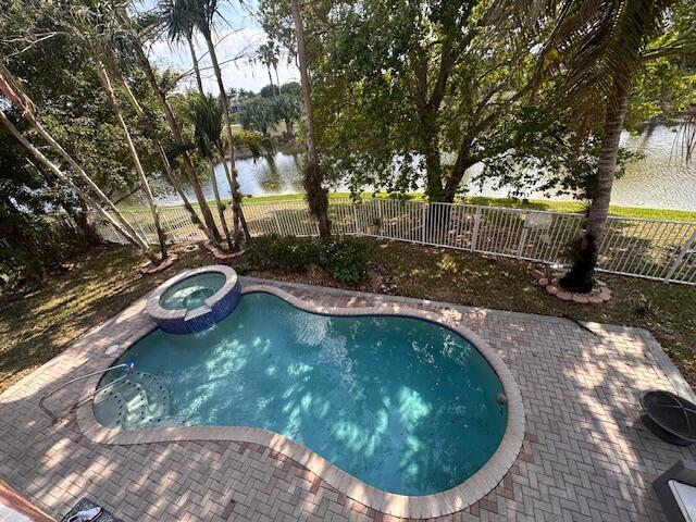 view of pool with a patio area, a pool with connected hot tub, a fenced backyard, and a water view