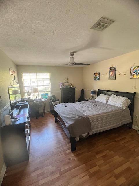 bedroom with visible vents, a textured ceiling, ceiling fan, and wood finished floors