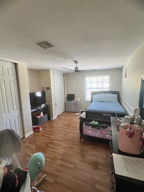 bedroom featuring visible vents, two closets, a textured ceiling, wood finished floors, and baseboards