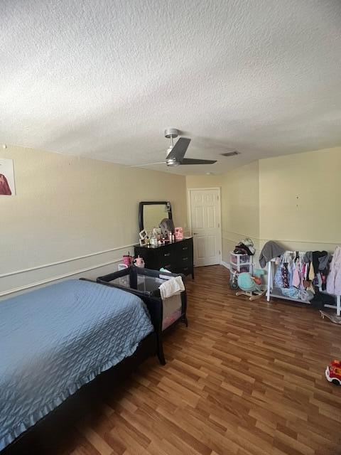 bedroom with a ceiling fan, wood finished floors, visible vents, and a textured ceiling