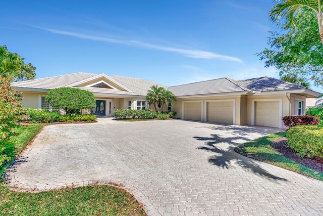 ranch-style house featuring stucco siding, an attached garage, a tile roof, and decorative driveway