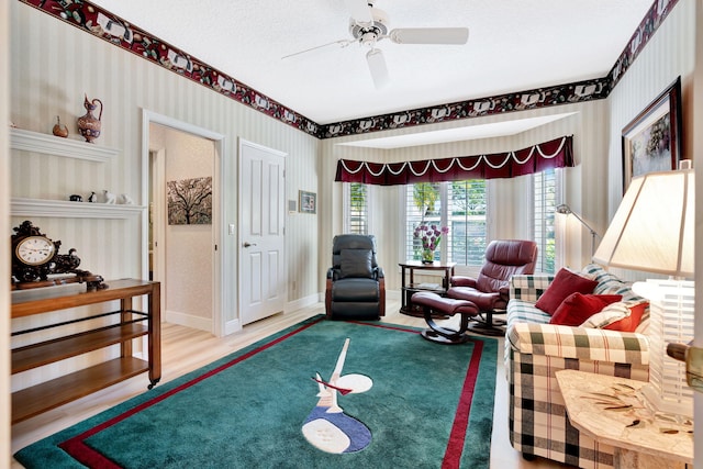 living area with wallpapered walls, ceiling fan, baseboards, wood finished floors, and a textured ceiling