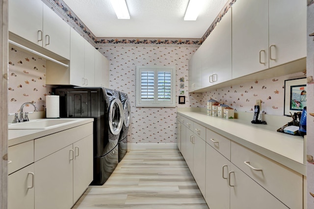 laundry area featuring a sink, washing machine and dryer, cabinet space, light wood-style floors, and wallpapered walls