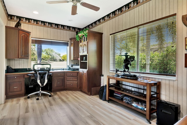 office area featuring light wood finished floors, built in study area, and a ceiling fan