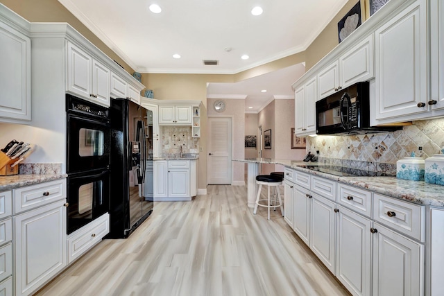 kitchen featuring light wood-style flooring, ornamental molding, decorative backsplash, black appliances, and white cabinets