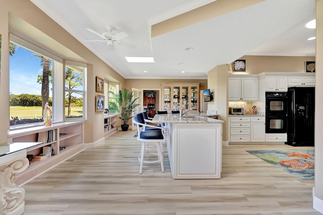 kitchen featuring black appliances, a breakfast bar, a ceiling fan, and ornamental molding