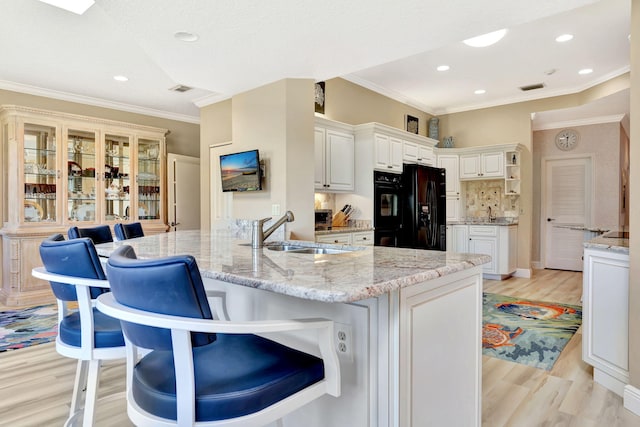 kitchen featuring light wood-style flooring, a sink, a kitchen breakfast bar, black fridge with ice dispenser, and crown molding